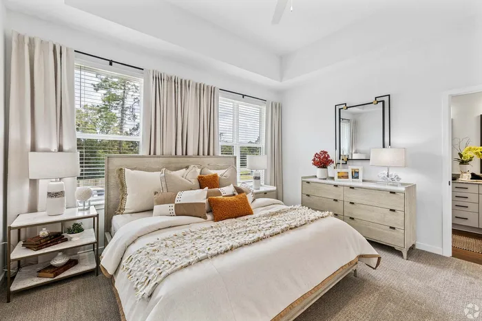 Elegant bedroom with modern decor, featuring a plush king-sized bed with stylish cushions, a spacious dresser, and large windows allowing abundant natural light.