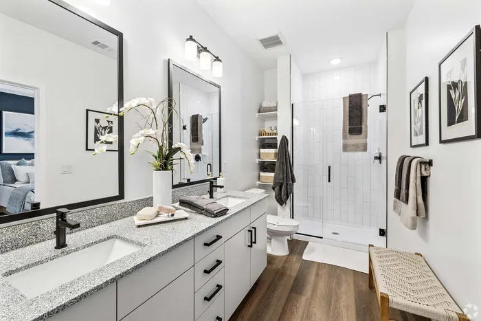Luxurious bathroom with dual sinks, elegant granite countertops, and spacious glass-enclosed shower. Modern decor and rich wooden floors create a serene oasis atmosphere.