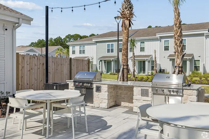 Charming outdoor patio with modern grill station and dining area, framed by picturesque palm trees and stylish townhouses in the background.