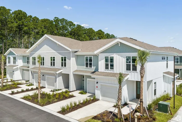 Charming townhouses with modern design, featuring individual driveways, garages, and lush greenery in a serene neighborhood setting.
