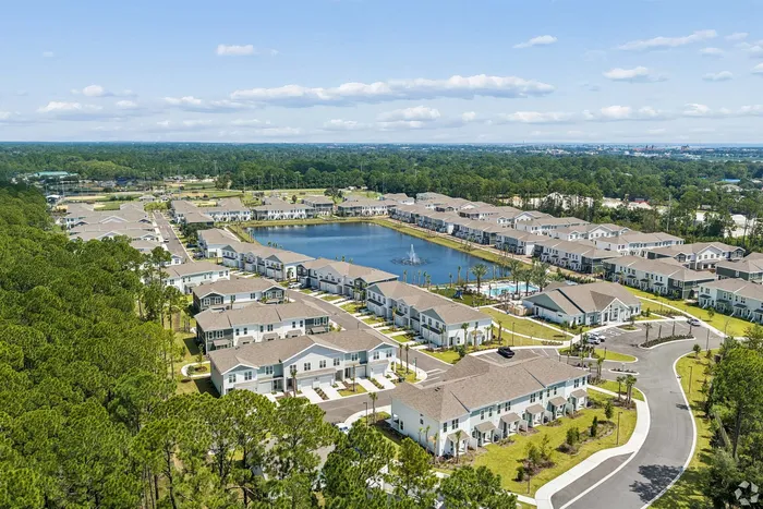 Expansive aerial view of a modern community with elegant homes, surrounding lush greenery and a serene lake centerpiece.