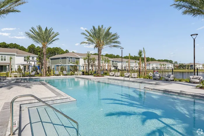 Luxurious community pool surrounded by palm trees and townhomes, offering a tropical oasis with plush poolside seating.