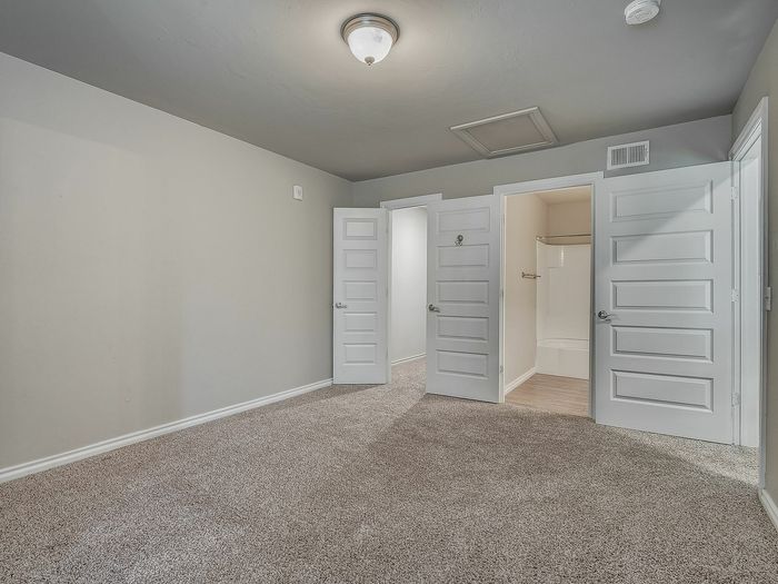 Inviting bedroom with plush carpeting, featuring elegant white paneled doors and an ensuite bathroom.