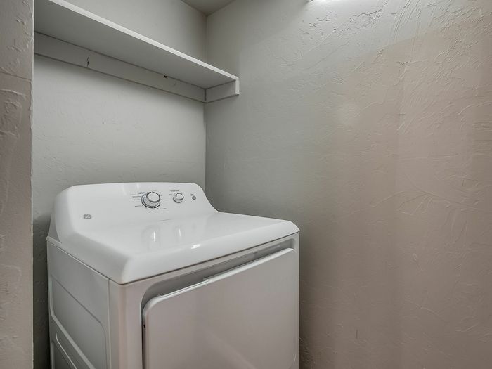 Cozy laundry area featuring a modern white washer with a convenient overhead shelf.