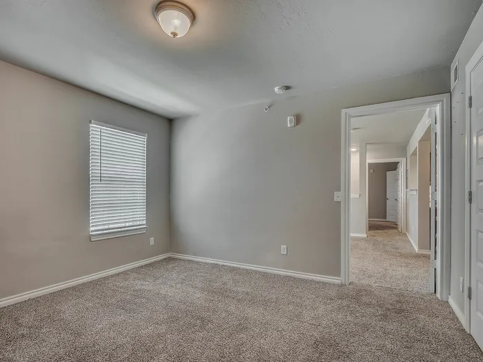 Inviting bedroom with soft carpet flooring, neutral walls, and ample natural light through a window with blinds.