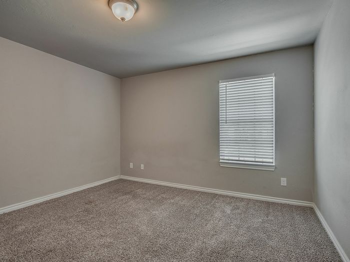 Inviting bedroom with neutral tones and plush carpeting, featuring a bright window with blinds.