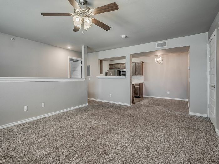 Inviting open-concept living room with plush carpet, ceiling fan, and a modern kitchenette.