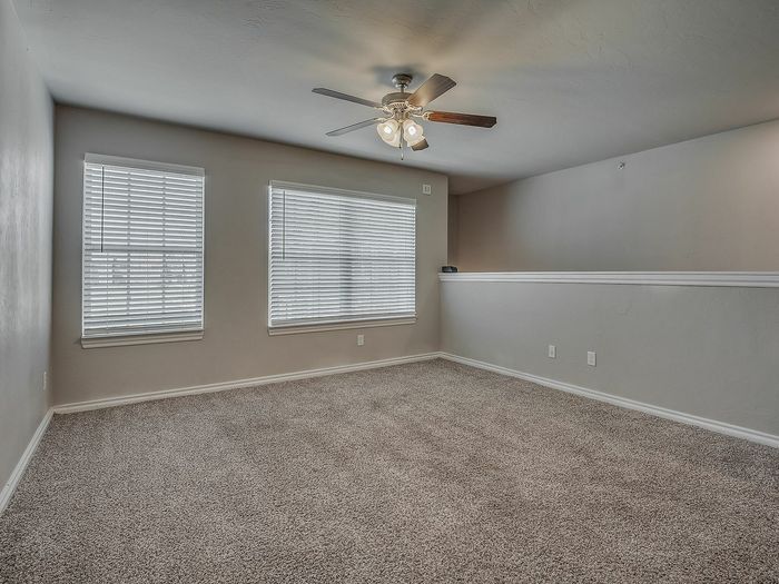 Bright, carpeted living room with large windows and ceiling fan.