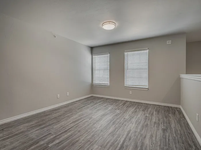 Bright, empty living room with modern gray flooring and large windows with blinds.