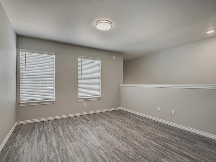 Modern room featuring sleek hardwood floors and large windows with blinds.