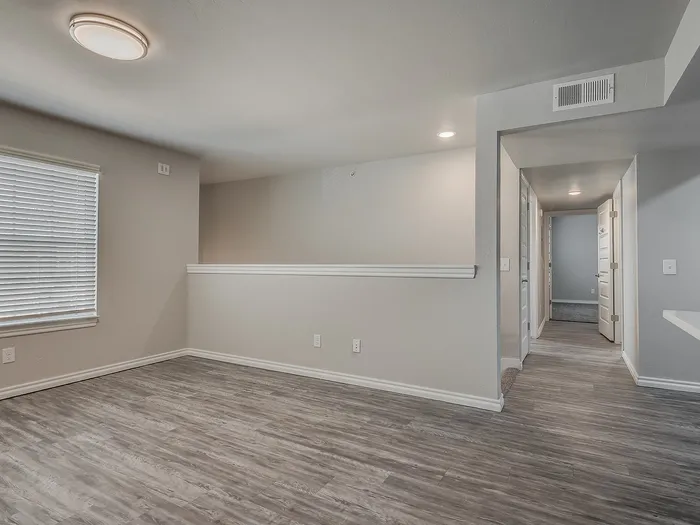 Spacious room with stylish wood flooring and soft natural light flowing through window blinds.