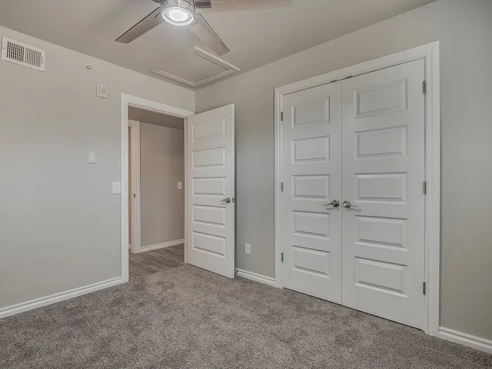 Inviting bedroom with soft carpet, elegant double doors, and modern ceiling fan.