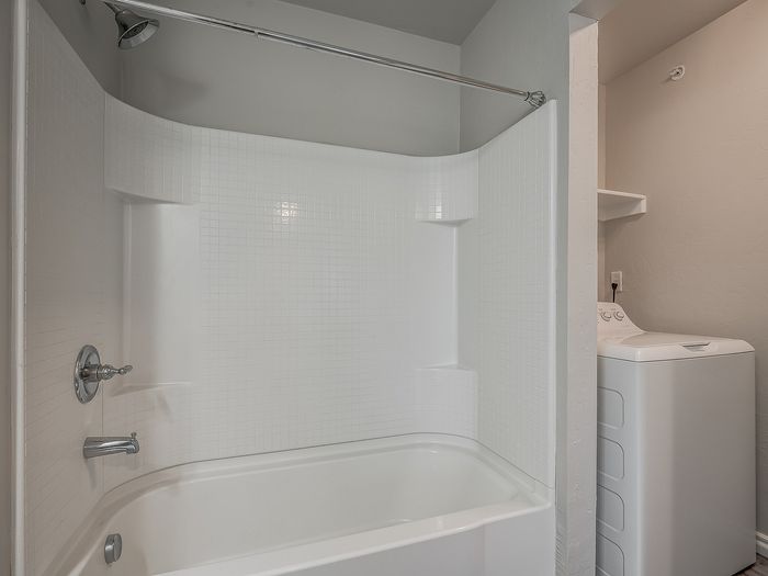 Sleek bathroom with modern bathtub and adjacent laundry area featuring a washing machine.