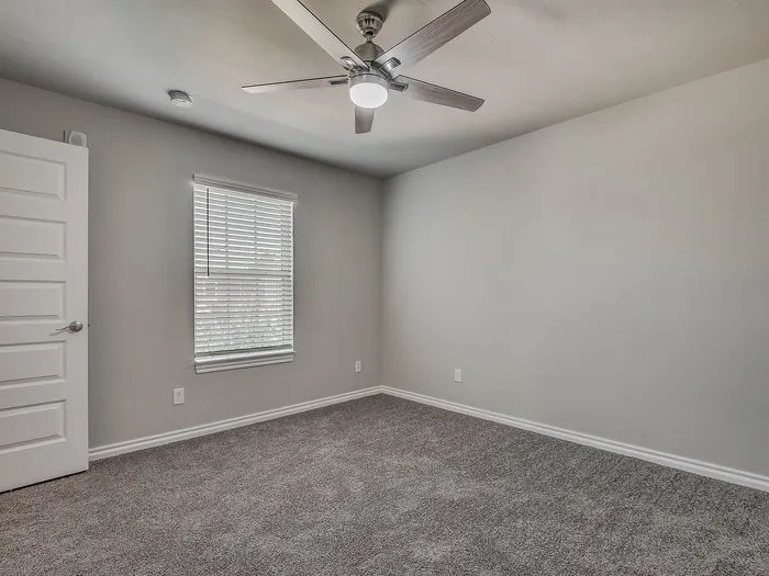 Bright and airy bedroom with soft carpet, modern ceiling fan, and large window with blinds.