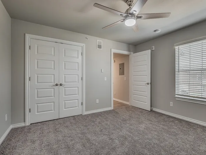 Bright bedroom with plush carpet, double doors, and ceiling fan.