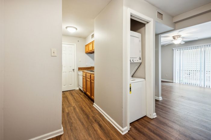 Bright apartment interior showcasing a sleek kitchen with wooden cabinets, modern appliances, and in-unit laundry, leading to a spacious living area with large patio doors.
