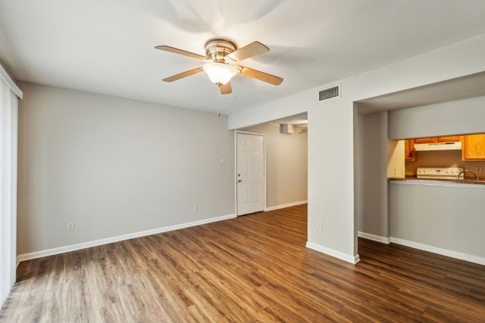 Bright and airy living space with elegant wood flooring, modern ceiling fan, and an inviting open kitchen layout.