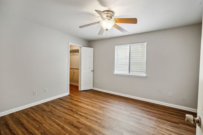 Bright bedroom featuring rich hardwood floors, a large window, ceiling fan, and a spacious walk-in closet.