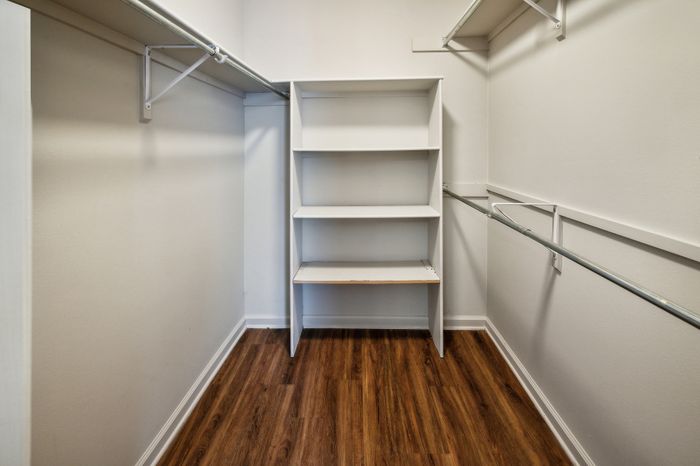 Spacious walk-in closet with elegant wooden flooring and built-in shelving.