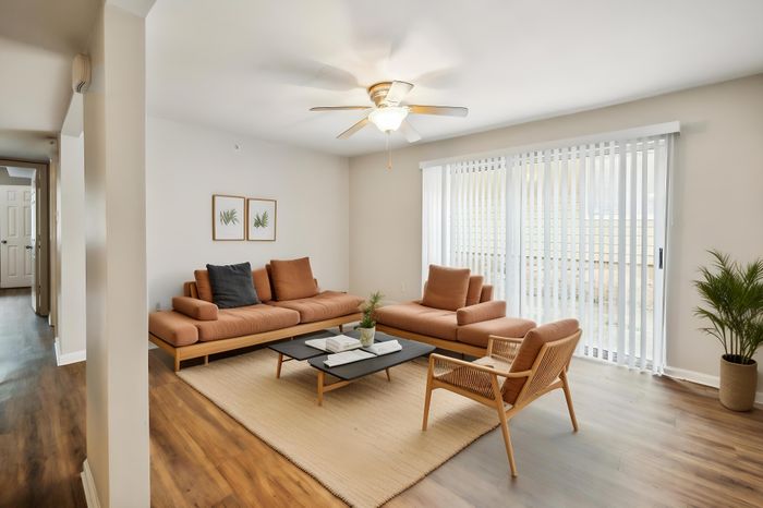 Bright and inviting living room with modern tan sofas, hardwood flooring, and abundant natural light streaming through sliding glass doors.