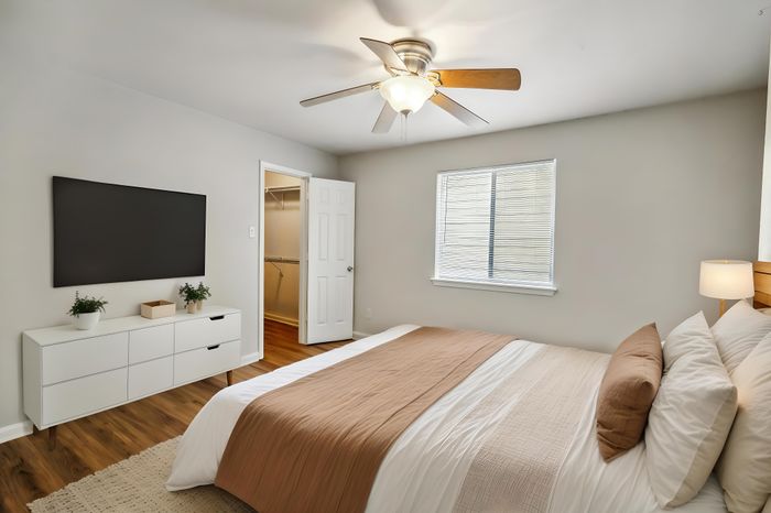 Inviting bedroom with elegant wood floors, a ceiling fan, and a spacious walk-in closet, perfect for comfort and style.