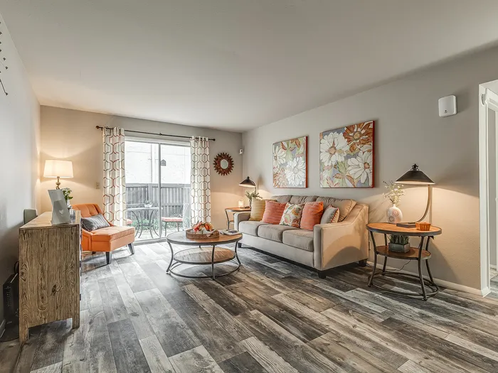 Bright and inviting living room with modern wooden flooring, elegant couch, vibrant decor, and natural light from sliding patio doors.