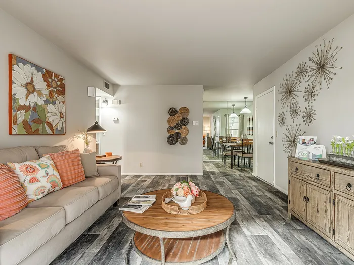 Charming living room with cozy sofa, vibrant cushions, and artistic decor leading to a stylish dining area.