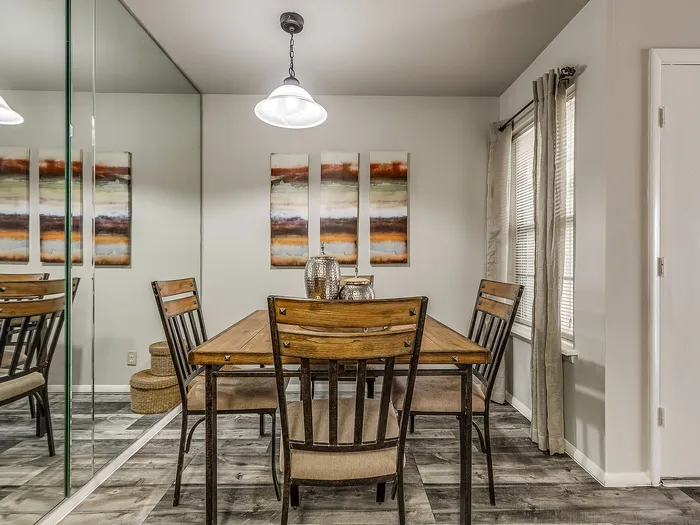 Charming dining area with rustic wooden table, elegant chairs, and modern decor reflected in a large mirror.