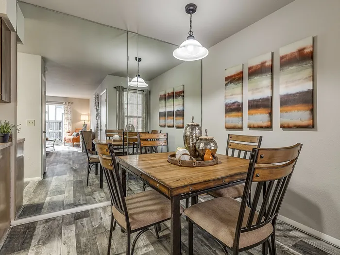 Elegant dining area with a wooden table set, artistic wall decor, and a mirrored wall reflecting modern living room space.
