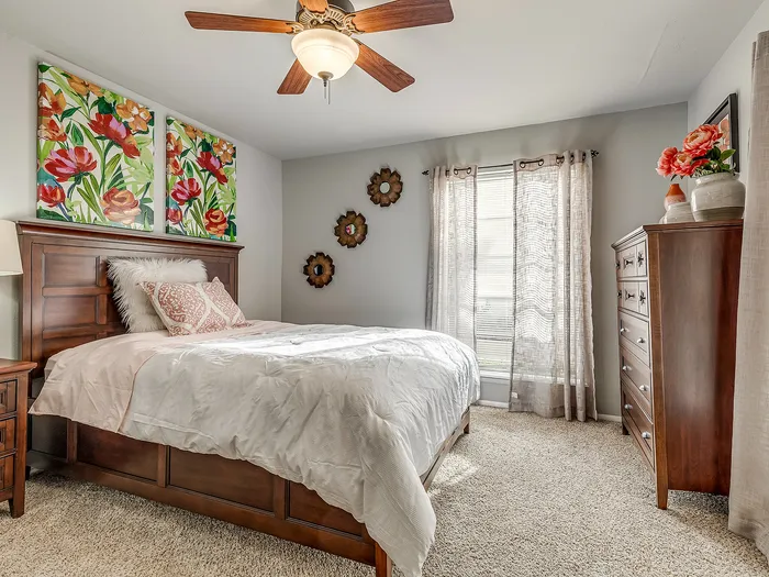 Inviting bedroom featuring elegant wooden furniture, chic floral artwork, and abundant natural light through sheer curtains.