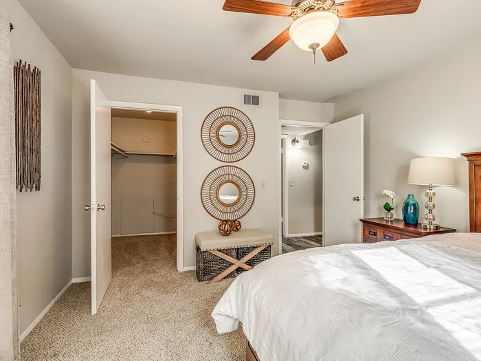 Bright and inviting bedroom with a cozy walk-in closet, stylish decor, and modern ceiling fan.