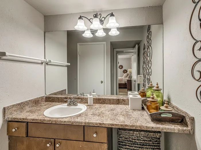 Chic bathroom with modern lighting, mirror, and elegant vanity setup leading to a cozy bedroom.