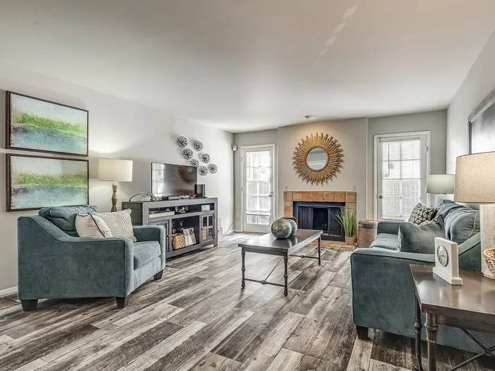 Inviting living room with stylish decor, featuring plush blue seating, modern art, a sleek TV console, and a cozy fireplace accentuated by elegant accents.