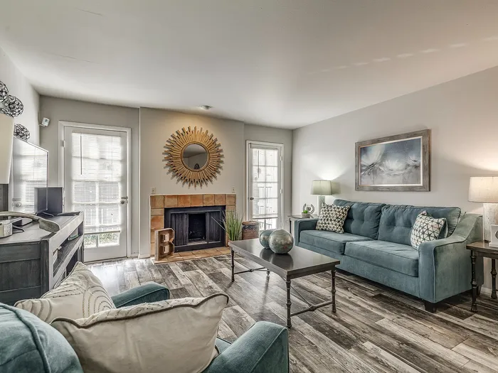 Inviting living room featuring a modern teal sofa, elegant fireplace, and a chic sunburst mirror with abundant natural light.