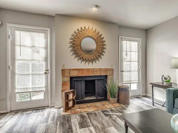 Charming living room with modern sunburst mirror, cozy fireplace, and elegant French doors, complemented by stylish wood flooring.