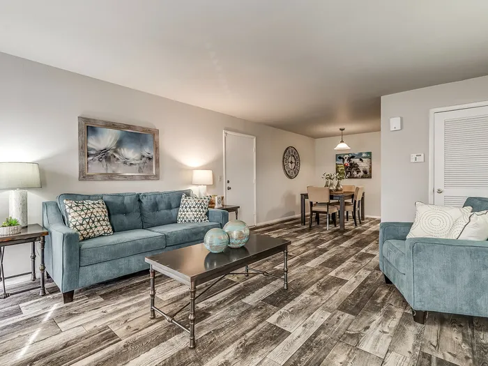 Elegant living room with stylish decor, featuring a cozy teal sofa, contemporary coffee table, and open dining area with rustic wood flooring.