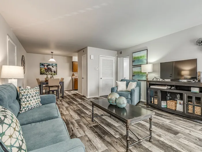Inviting living room with stylish decor, featuring a cozy blue sofa, sleek wooden floors, and a modern entertainment center, leading to a charming dining space.