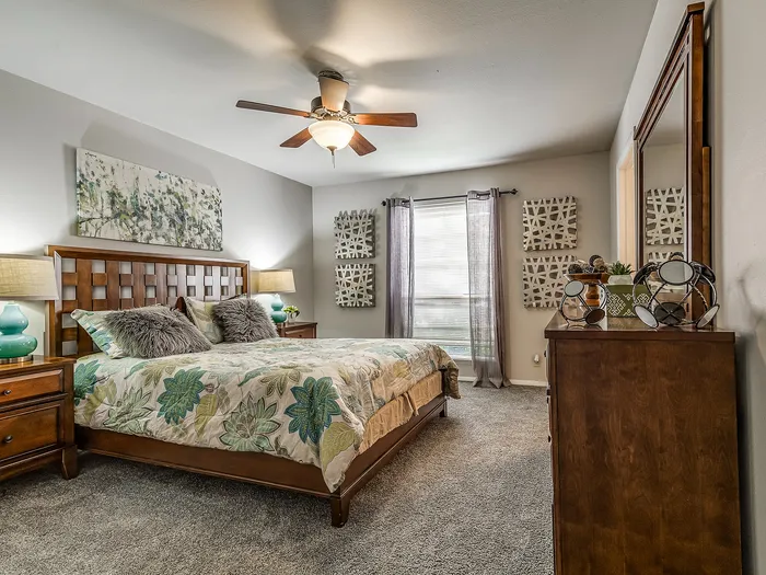 Inviting bedroom with a luxurious floral bedspread, elegant wooden furniture, and tranquil artwork creating a serene atmosphere.