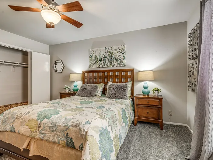 Inviting bedroom featuring a cozy bed with floral bedding, elegant wood furniture, and stylish decor under a modern ceiling fan.