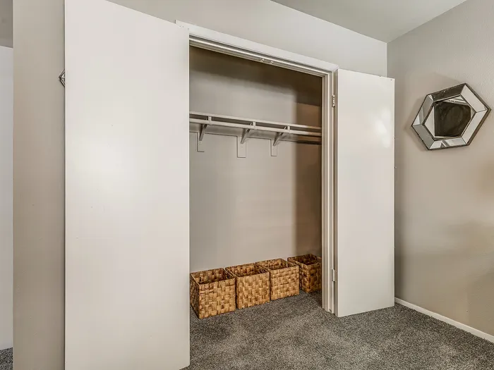Spacious wardrobe with open doors revealing ample shelving and stylish woven baskets, set against a modern gray interior.