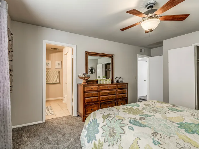 Inviting bedroom with elegant wooden dresser and floral bedding, leading to a connected modern bathroom.