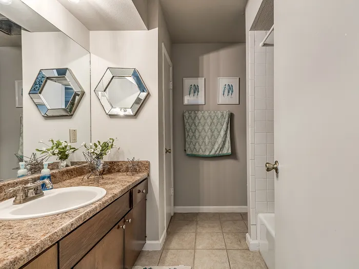 Elegant bathroom with a luxurious marble countertop, stylish hexagonal mirrors, and framed artwork creating a serene ambiance.