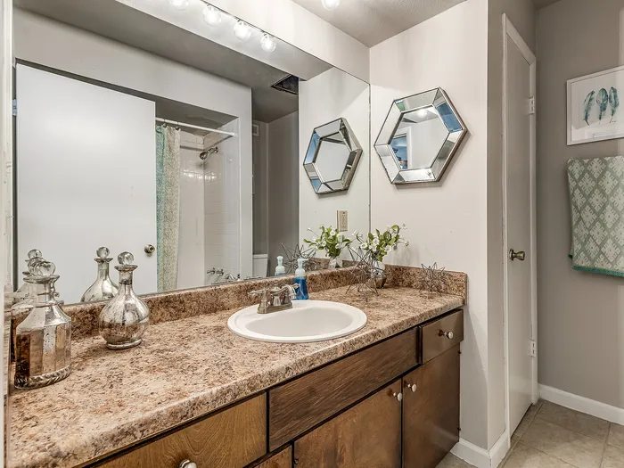 Elegant bathroom with a chic marble countertop, modern fixtures, and decorative accents, featuring a large mirror and stylish wall decor.