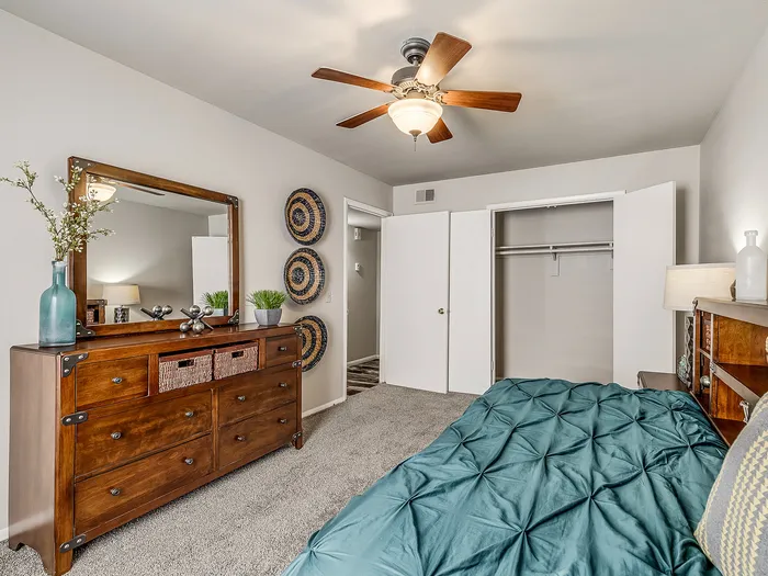 Inviting bedroom showcasing a modern ceiling fan, elegant wooden dresser with decorative items, and open closet space.