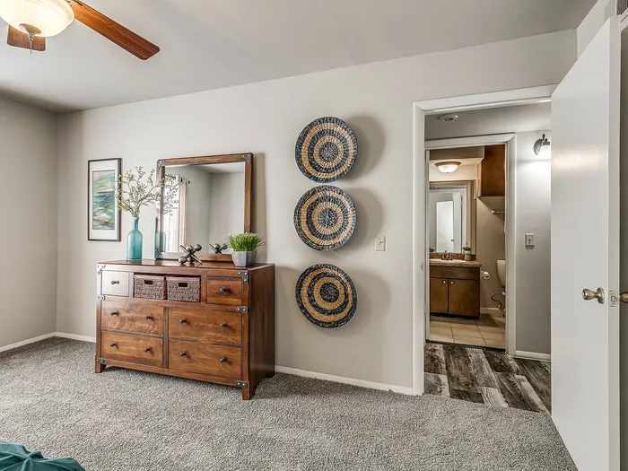 Inviting bedroom with elegant wooden dresser, stylish wall decor, and access to a modern bathroom.