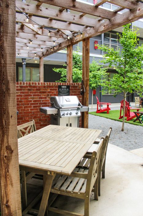 Charming outdoor patio with a rustic wooden pergola, elegant dining set, and modern grill in a lush courtyard setting.