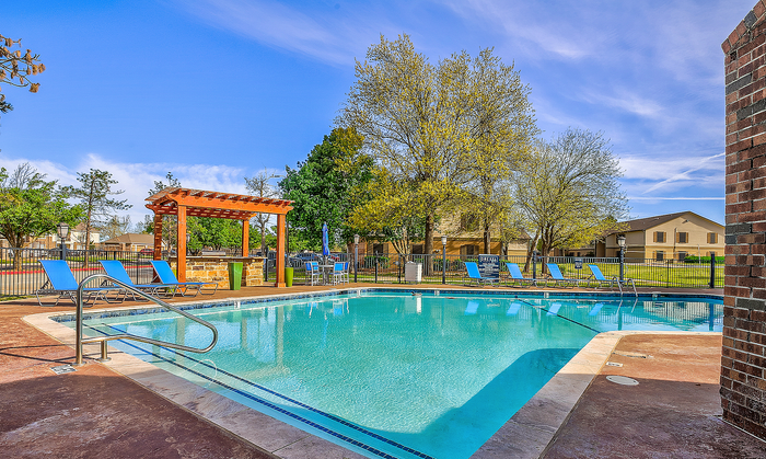 Inviting outdoor pool area with modern lounge chairs and charming pergola, set against a scenic backdrop of trees and residential homes.