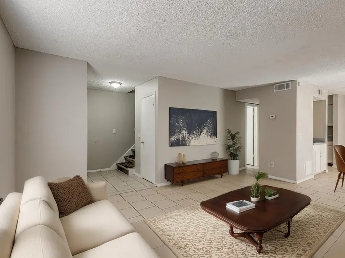 Inviting living room with modern decor, featuring a cozy beige sofa, chic coffee table, elegant artwork, and lush indoor plants, creating a warm and welcoming atmosphere.