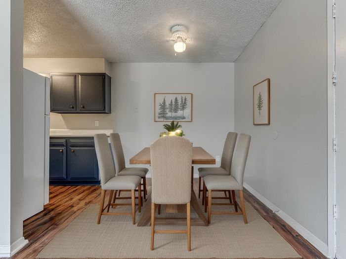 Elegant dining area with a modern table and six beige chairs, adjacent to a cozy kitchen with stylish dark cabinets.