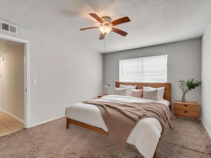Inviting bedroom with plush carpeting, cozy wooden bed, and elegant ceiling fan, perfect for relaxation.